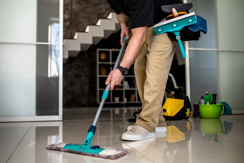 Hombre limpiando el suelo con un trapeador en un ambiente moderno, rodeado de herramientas de limpieza, como un balde y productos de limpieza.